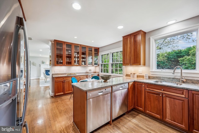 kitchen featuring a peninsula, light stone countertops, a sink, light wood finished floors, and appliances with stainless steel finishes
