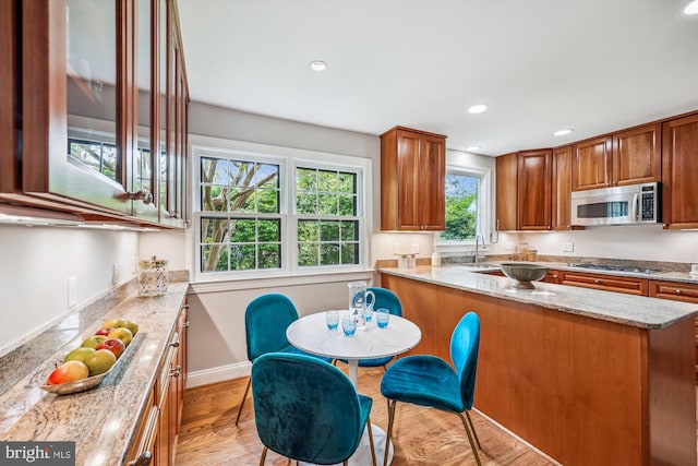 kitchen with appliances with stainless steel finishes, brown cabinetry, light stone counters, and light wood finished floors