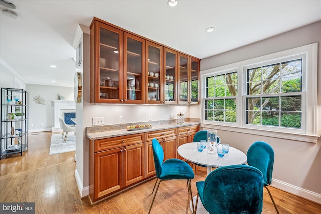 kitchen with brown cabinets, light stone counters, light wood finished floors, baseboards, and glass insert cabinets