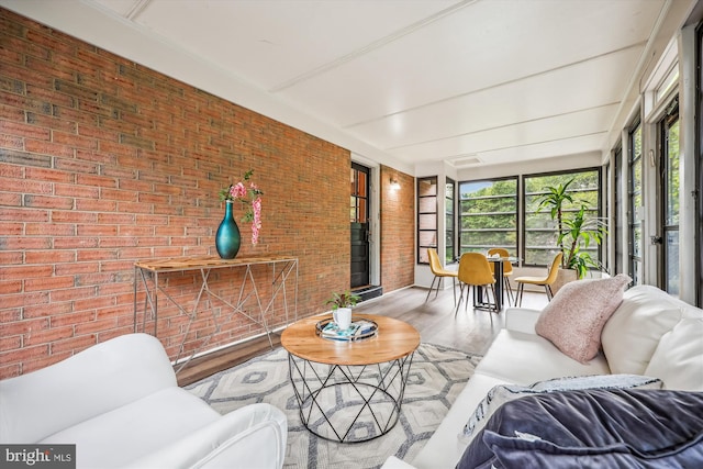 sunroom / solarium featuring wood finished floors and brick wall
