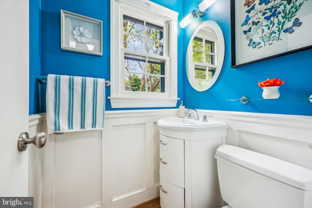 bathroom featuring vanity, a wainscoted wall, a decorative wall, and toilet