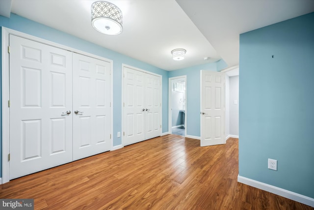unfurnished bedroom with multiple closets, baseboards, and wood finished floors