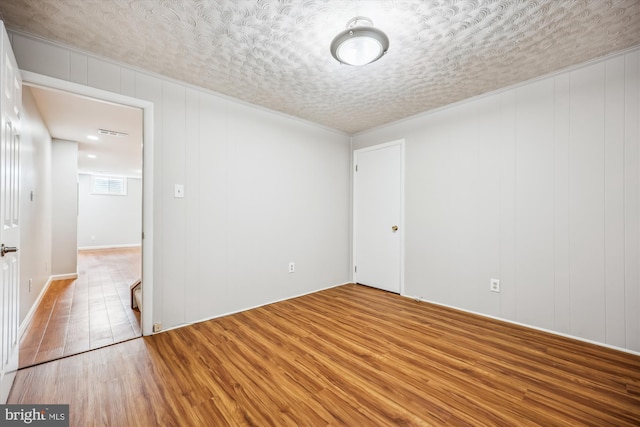 spare room with crown molding, a textured ceiling, visible vents, and wood finished floors