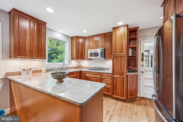 kitchen featuring brown cabinets, appliances with stainless steel finishes, a sink, a peninsula, and light wood-type flooring