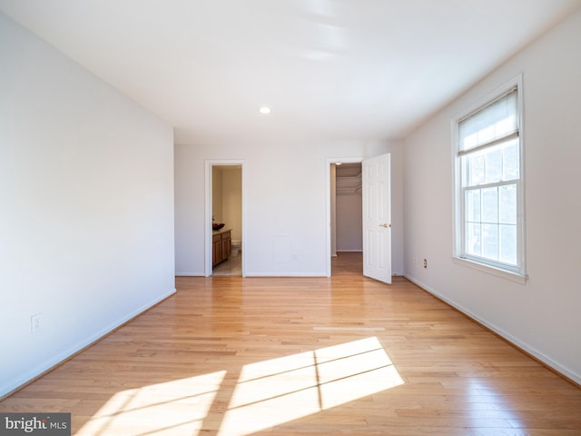 unfurnished bedroom featuring ensuite bathroom, a walk in closet, a closet, and light hardwood / wood-style flooring