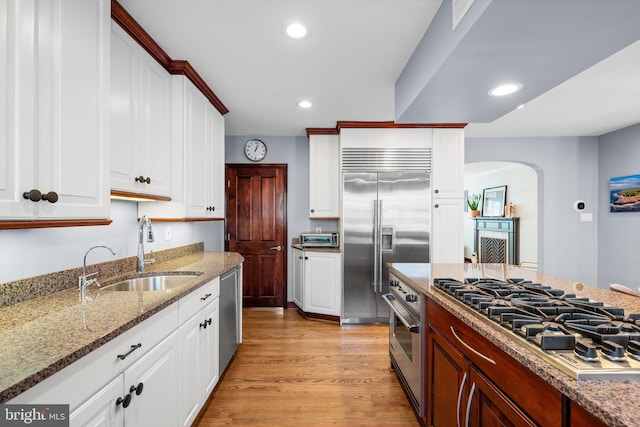 kitchen with appliances with stainless steel finishes, white cabinetry, sink, light stone counters, and light hardwood / wood-style floors