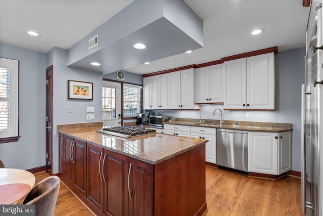 kitchen featuring appliances with stainless steel finishes, sink, white cabinets, light hardwood / wood-style floors, and light stone countertops