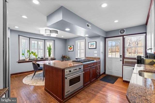 kitchen with stainless steel appliances, wood-type flooring, light stone countertops, and sink