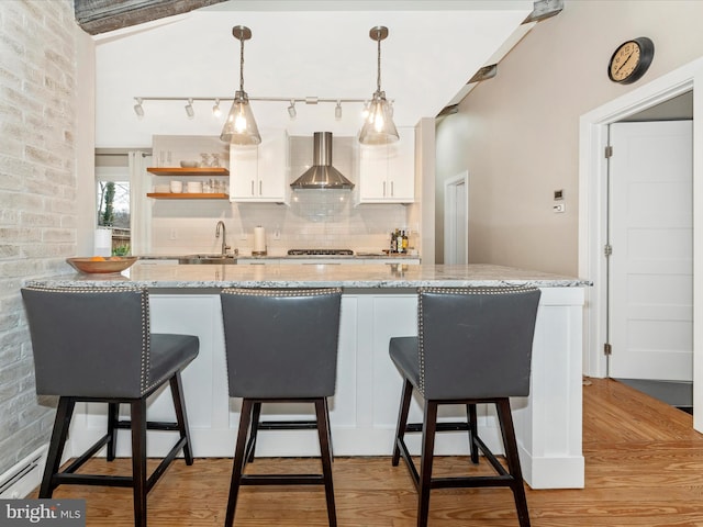 kitchen with wall chimney exhaust hood, sink, light stone counters, pendant lighting, and white cabinets