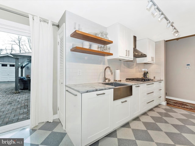 kitchen featuring stainless steel gas cooktop, sink, white cabinets, light stone countertops, and backsplash