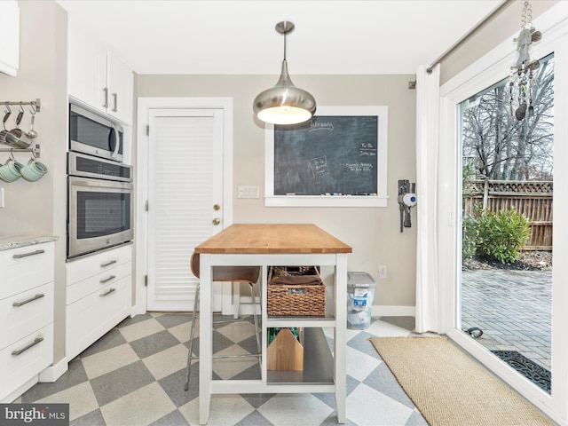 kitchen with hanging light fixtures, white cabinetry, appliances with stainless steel finishes, and light stone countertops