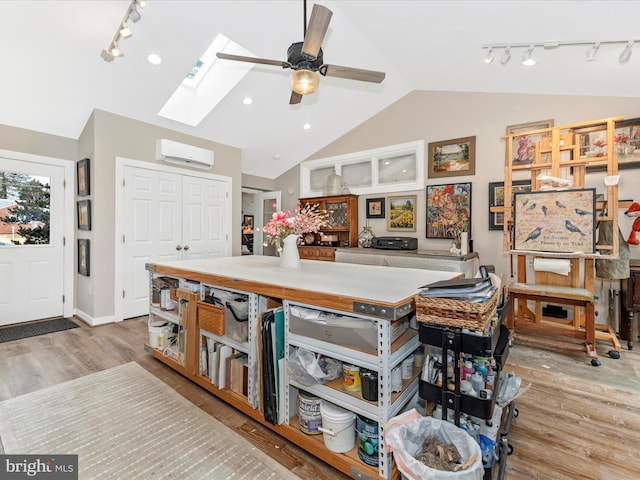 interior space with a wall unit AC, lofted ceiling with skylight, light hardwood / wood-style floors, and ceiling fan