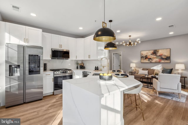 kitchen with white cabinetry, hanging light fixtures, light stone countertops, and appliances with stainless steel finishes