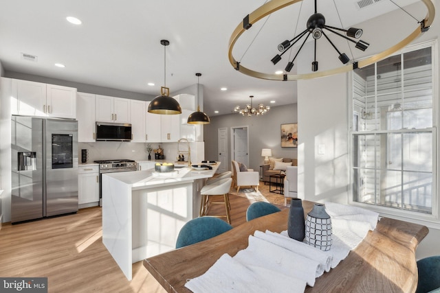 kitchen featuring an inviting chandelier, hanging light fixtures, stainless steel appliances, white cabinets, and decorative backsplash