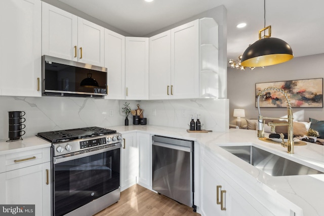 kitchen with decorative light fixtures, tasteful backsplash, white cabinetry, stainless steel appliances, and light stone countertops