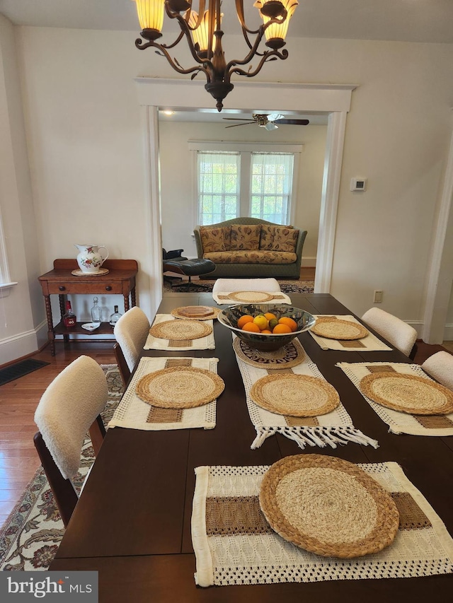 dining area featuring baseboards, visible vents, wood finished floors, and ceiling fan with notable chandelier