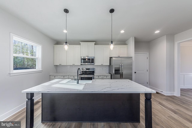 kitchen with stainless steel appliances, a kitchen island with sink, hanging light fixtures, and white cabinets