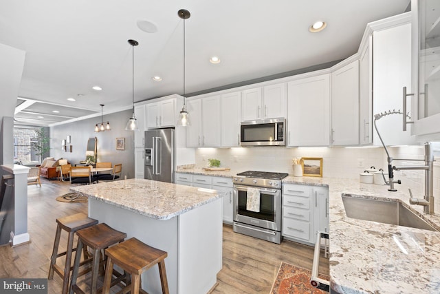 kitchen featuring stainless steel appliances, a kitchen island, a sink, decorative backsplash, and light wood finished floors