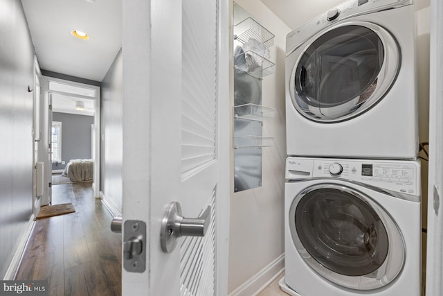 clothes washing area with laundry area, wood-type flooring, baseboards, and stacked washer and clothes dryer