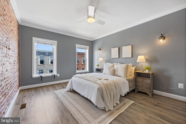 bedroom with visible vents, ornamental molding, brick wall, baseboards, and hardwood / wood-style flooring