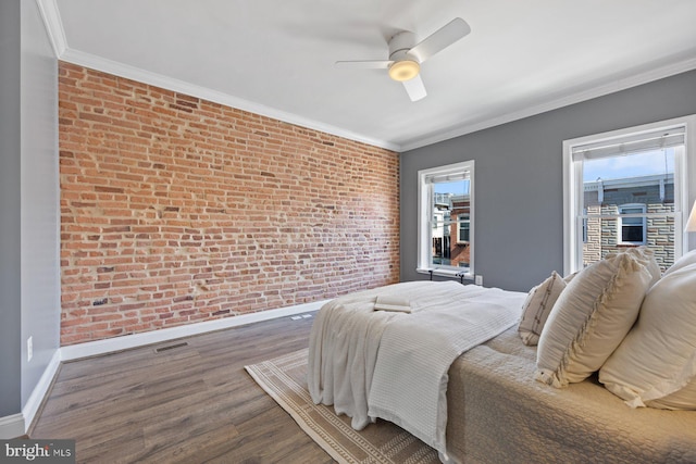 bedroom featuring crown molding, brick wall, wood finished floors, multiple windows, and baseboards