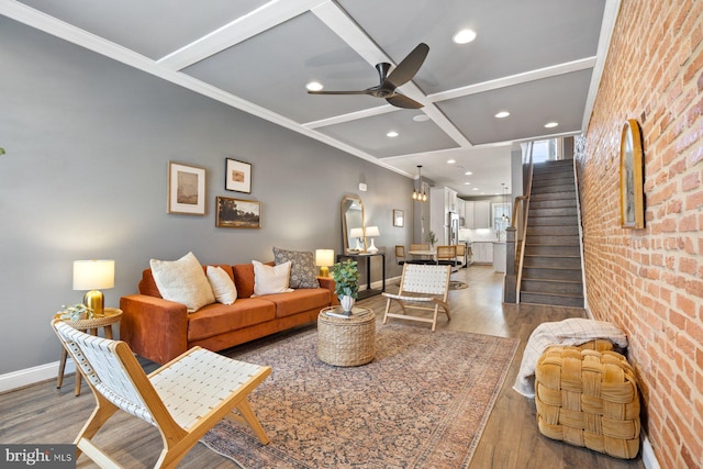 living area with brick wall, wood finished floors, coffered ceiling, baseboards, and stairs