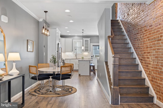 dining area featuring brick wall, baseboards, stairs, light wood-style floors, and ornamental molding