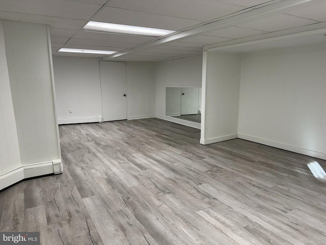 unfurnished room featuring baseboard heating, light hardwood / wood-style floors, and a drop ceiling