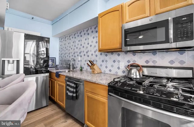 kitchen featuring sink, appliances with stainless steel finishes, backsplash, light stone counters, and light wood-type flooring