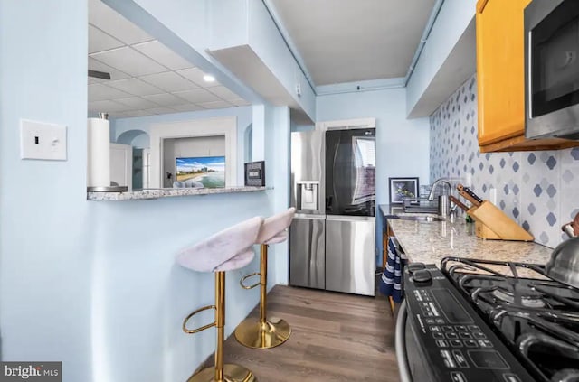 kitchen featuring sink, dark wood-type flooring, appliances with stainless steel finishes, light stone counters, and decorative backsplash