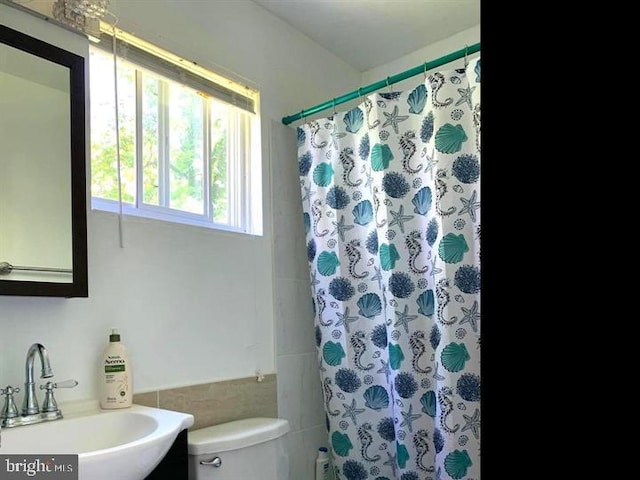 bathroom featuring walk in shower, sink, tile walls, and toilet