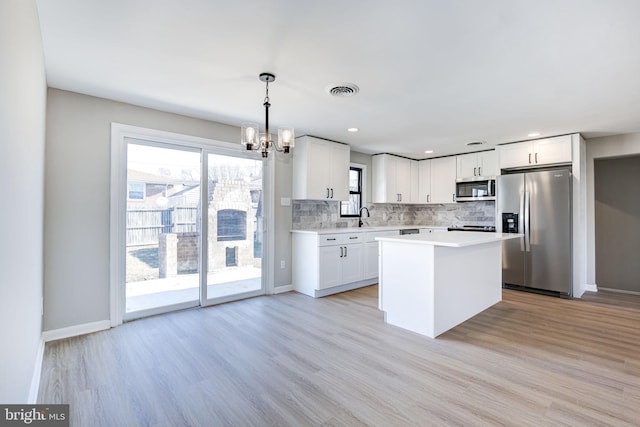 kitchen featuring a kitchen island, appliances with stainless steel finishes, decorative light fixtures, white cabinets, and backsplash