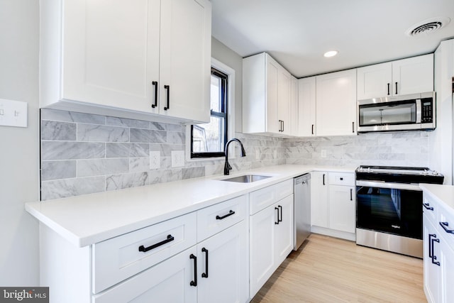 kitchen featuring appliances with stainless steel finishes, tasteful backsplash, sink, white cabinets, and light hardwood / wood-style flooring