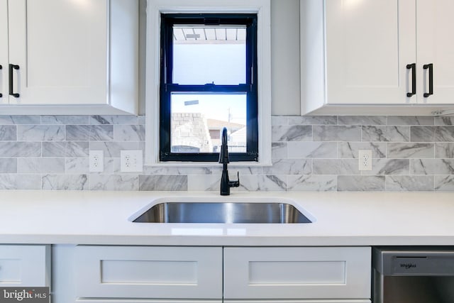 kitchen featuring dishwashing machine, sink, backsplash, and white cabinets