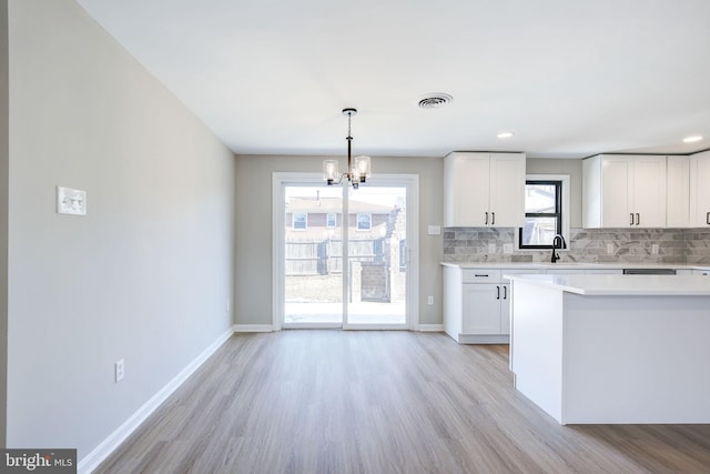 kitchen featuring white cabinetry, pendant lighting, light hardwood / wood-style flooring, and backsplash