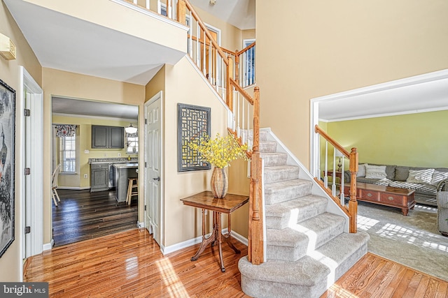 stairway with ornamental molding, wood-type flooring, and a high ceiling