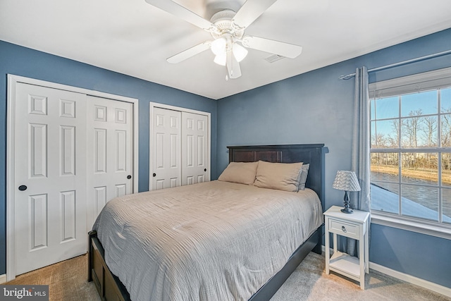 carpeted bedroom with two closets and ceiling fan