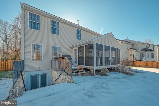 snow covered rear of property featuring a sunroom