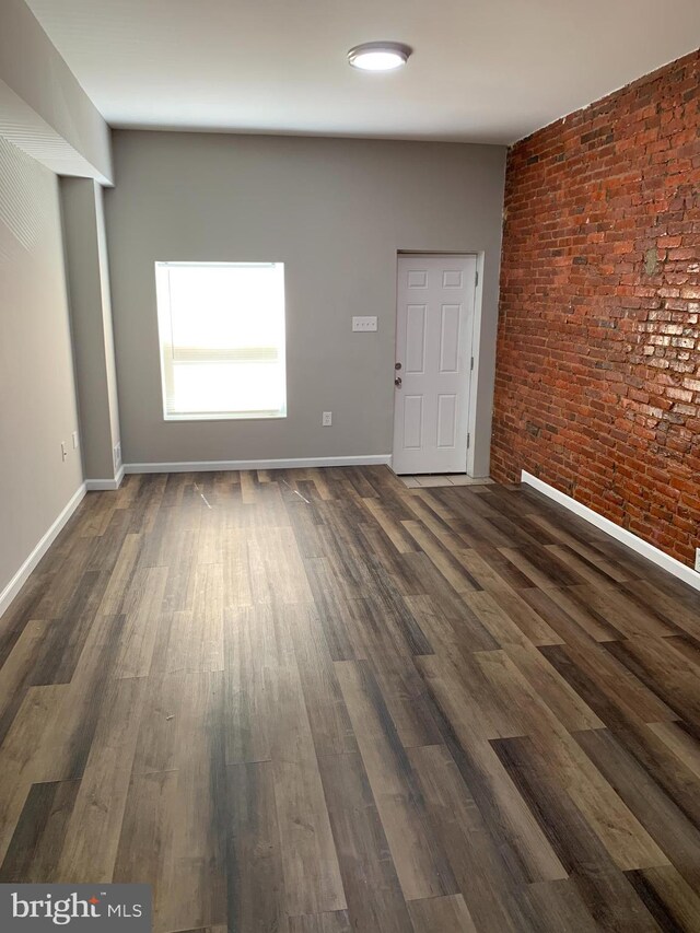 unfurnished room featuring brick wall and dark hardwood / wood-style floors