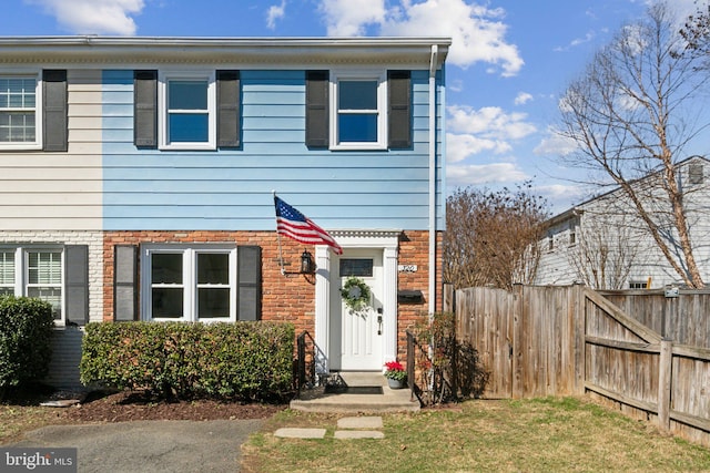 view of property featuring a front yard, brick siding, and fence