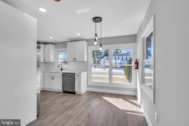 kitchen featuring sink, dishwasher, white cabinetry, hanging light fixtures, and light wood-type flooring