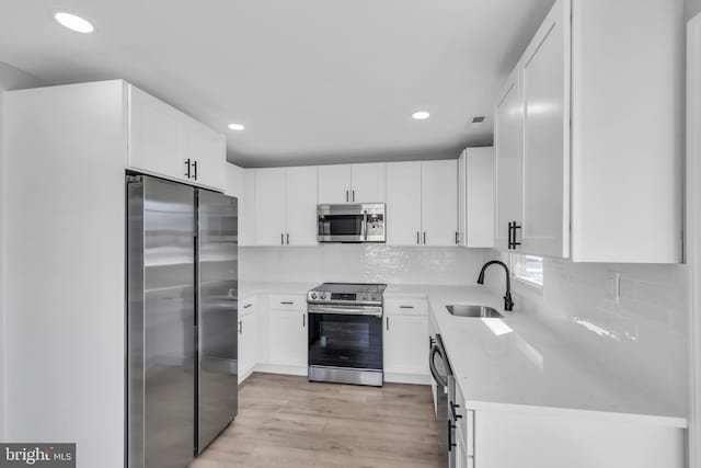 kitchen with white cabinetry, appliances with stainless steel finishes, sink, and light stone counters