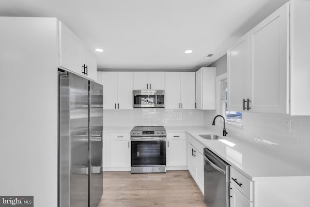 kitchen featuring sink, light wood-type flooring, appliances with stainless steel finishes, decorative backsplash, and white cabinets