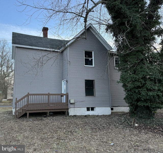 rear view of house with a wooden deck, a chimney, and roof with shingles