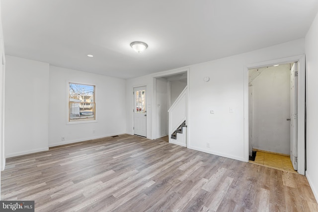 unfurnished room with stairway, light wood-type flooring, and baseboards