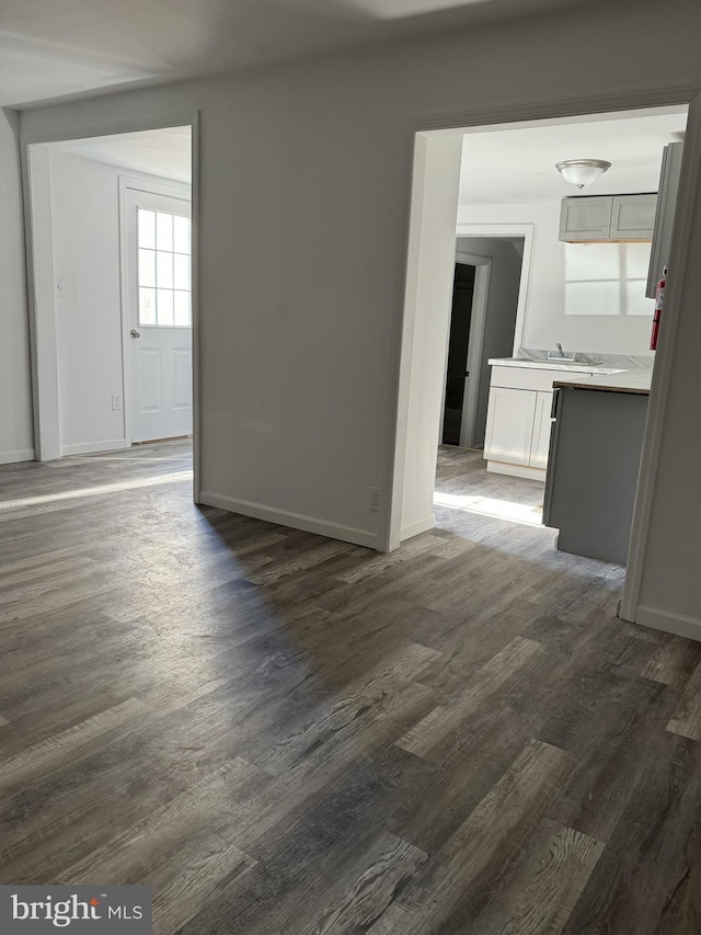 empty room with dark wood-type flooring, baseboards, and a sink