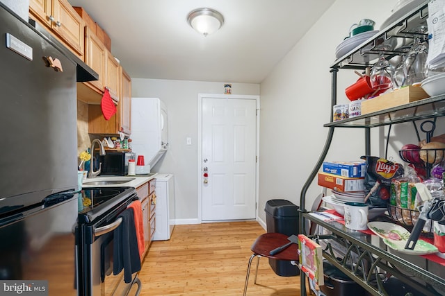 kitchen with stainless steel refrigerator, sink, stacked washer and dryer, light brown cabinets, and light wood-type flooring