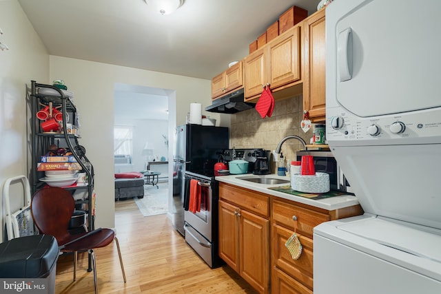 kitchen featuring tasteful backsplash, sink, stainless steel range with electric cooktop, stacked washer / drying machine, and light hardwood / wood-style flooring