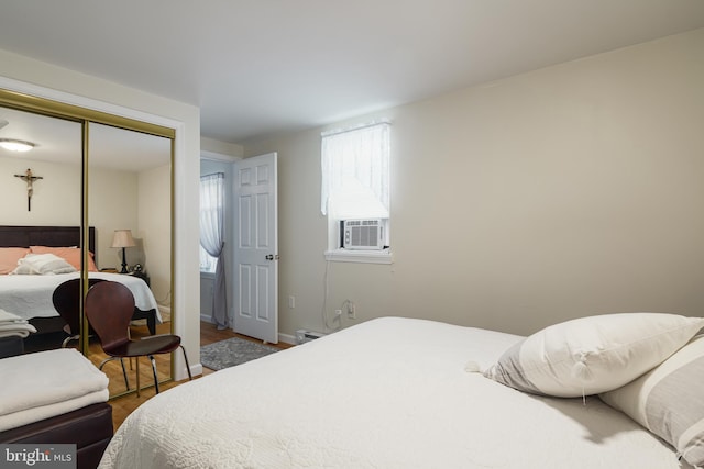 bedroom with cooling unit, hardwood / wood-style floors, a baseboard radiator, and a closet