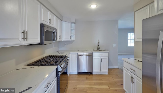 kitchen featuring stainless steel appliances, white cabinetry, sink, and light stone counters